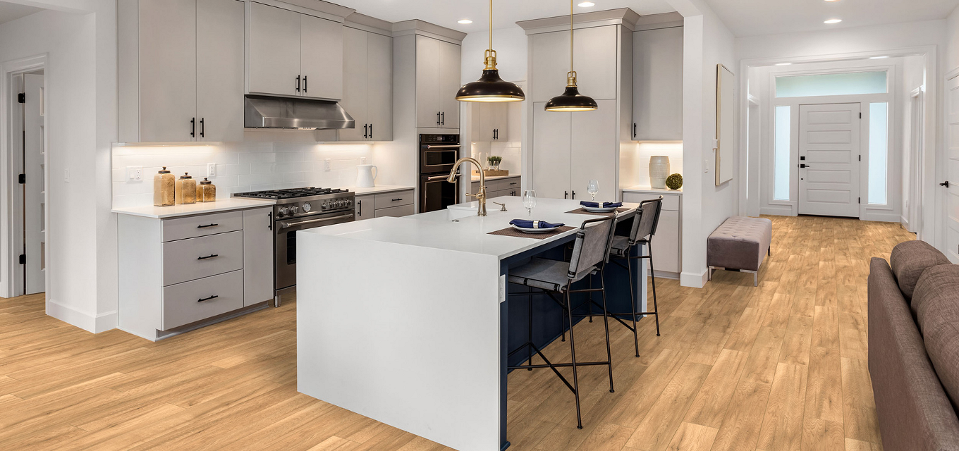 A kitchen with a center island next to a living room featuring Spc Flooring's Z209 Butterscotch oak.